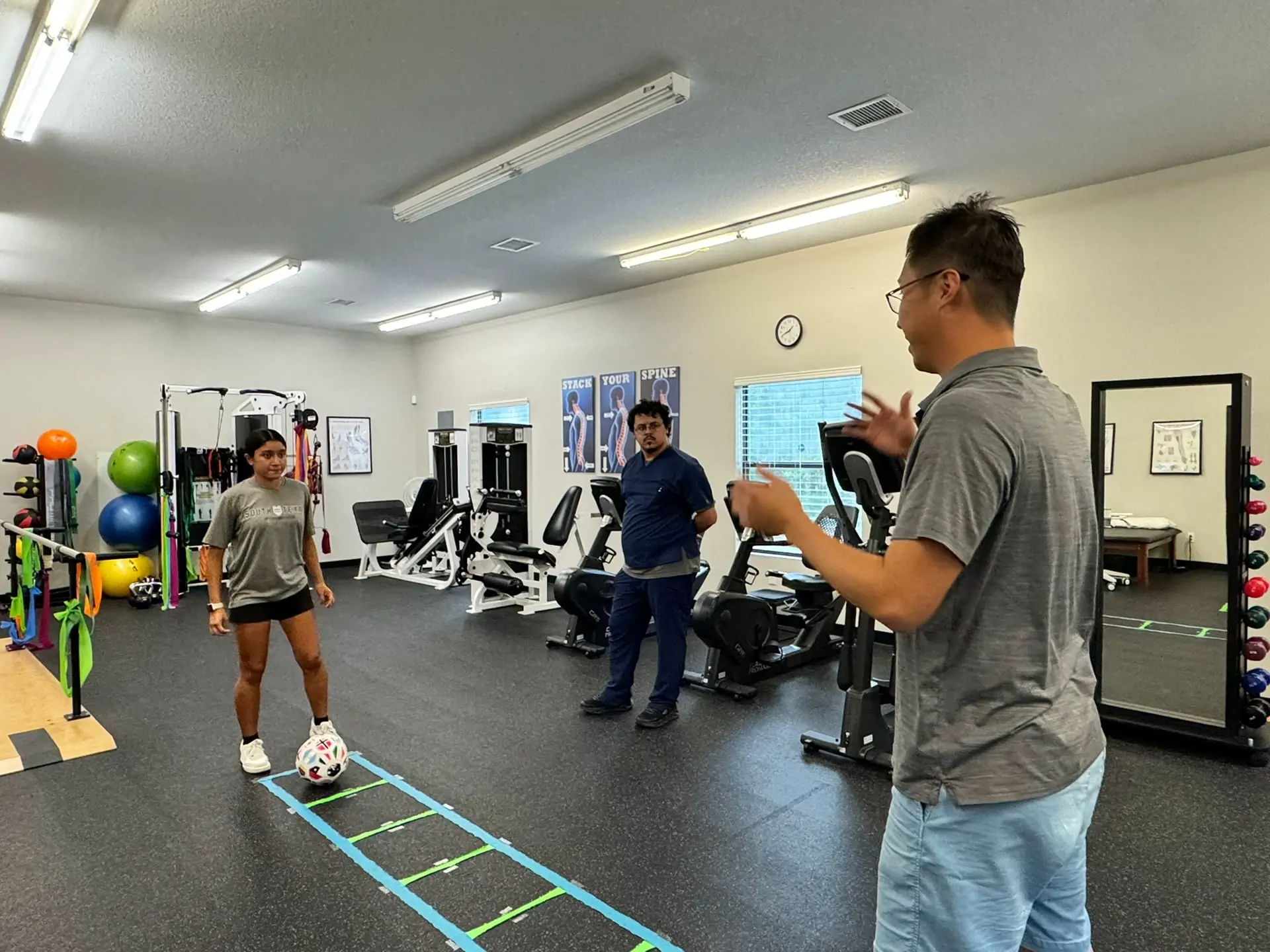 The open treatment floor at Direct PT of Huntsville: cable machine, resistance bands, exercise balls and a colour-taped agility ladder on rubber flooring.