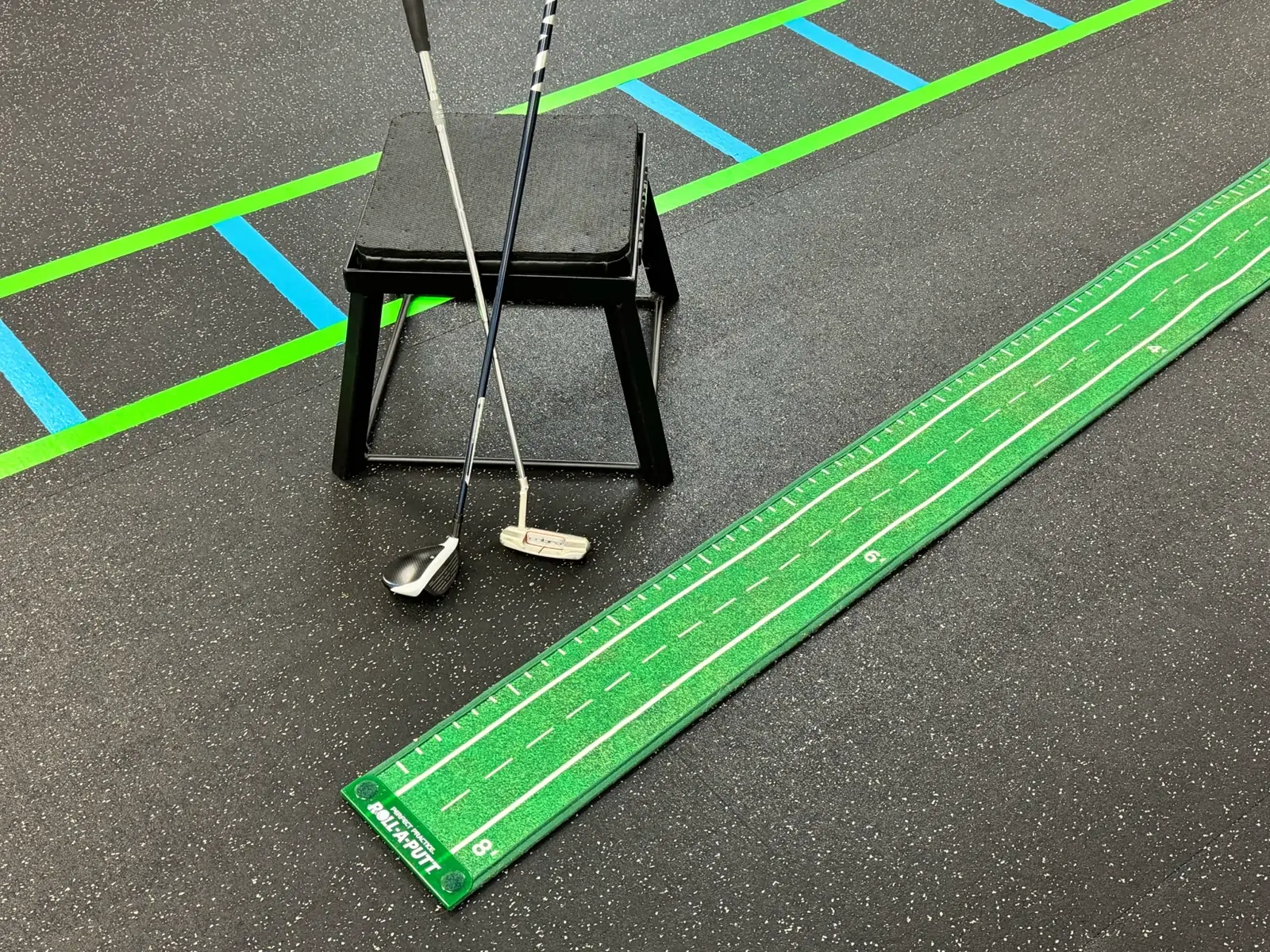 A putter and golf ball on a practice green laid across the clinic floor beside the agility ladder.