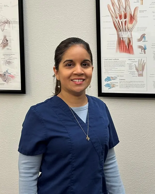 Florencia Chacon, PT Tech, in navy scrubs beside a hand and wrist anatomy chart at Direct PT of Huntsville.