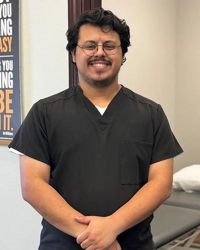 Tony Delclos, PTA, smiling in black scrubs in a treatment room at Direct PT of Huntsville.